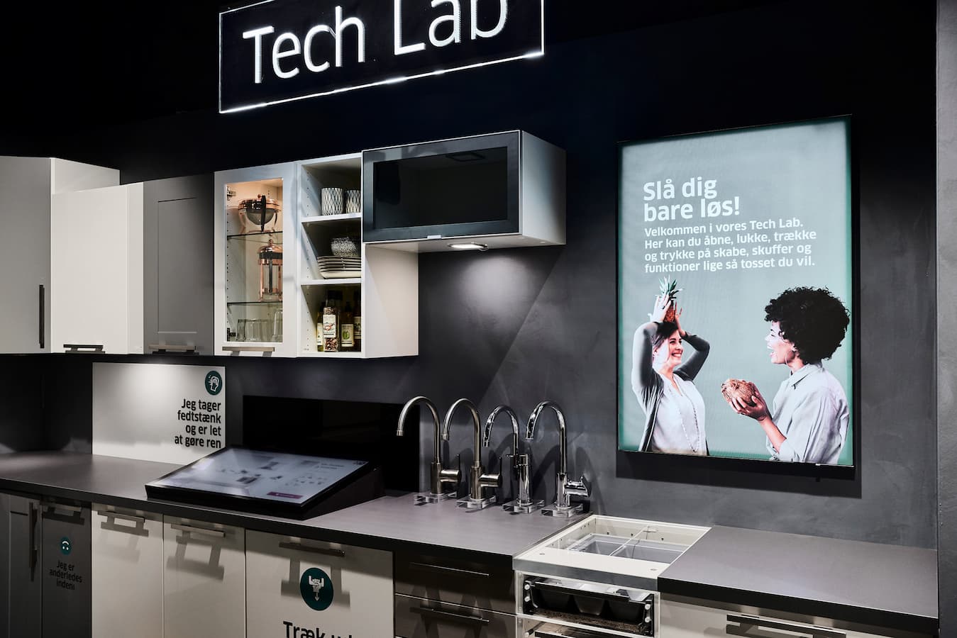 Tech Lab-køkkenudstilling med belyst kampagneplakat og grafisk skiltning
